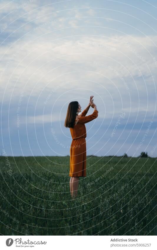 Frau in orangefarbenem Kleid genießt die Natur auf einer grünen Wiese Feld Himmel Wolken im Freien gestikulieren brünett Sommer Gras Mode Gelassenheit friedlich