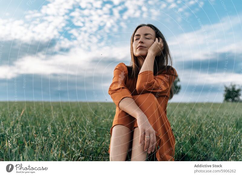 Gelassene Frau in orangefarbenem Kleid genießt die Natur in einem Feld Gelassenheit brünett orangefarbenes Kleid Augen geschlossen beschaulich im Freien grün