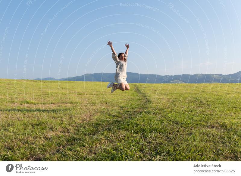 Freudig springende Frau auf einer weiten grünen Wiese Freude Freiheit Glück Feier Feld Berge u. Gebirge Gelassenheit im Freien Natur Sommer Himmel Landschaft