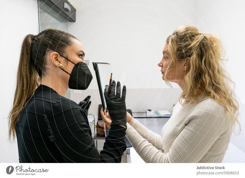 Kosmetikerin erklärt einer Kundin das Microblading-Verfahren Klient Mikroschneiden Behandlung skizzierend Messung Schönheit Augenbraue Gesichtsbehandlung