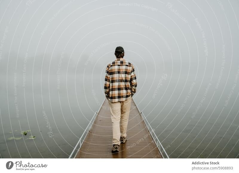 Mann spaziert auf nebligem Pier in ruhiger Naturszene laufen Nebel Gelassenheit hölzern geheimnisvoll unkenntlich anonym gesichtslos Rückansicht Morgen