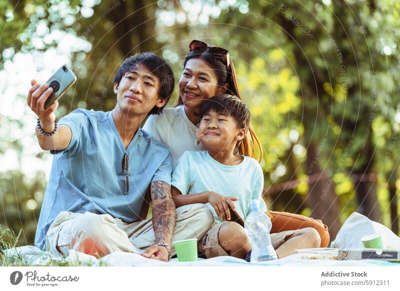 Asiatische Familie genießt ein sonniges Picknick mit einem Selfie Moment asiatisch Sommer Park im Freien heiter Freude Fröhlichkeit Erholung Freizeit Bonden