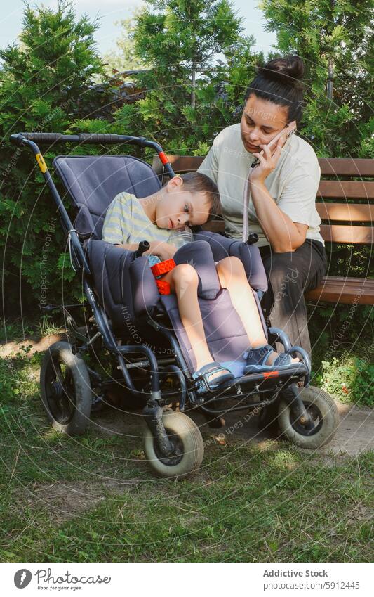 Mutter, die ihren Sohn mit zerebraler Lähmung im Freien pflegt zerebrale Kinderlähmung Rollstuhl Park Pflege Behinderung Liebe Zuneigung Aufmerksamkeit