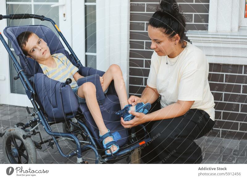 Mutter passt Schuhe für Sohn im Rollstuhl im Freien an zerebrale Kinderlähmung Behinderung Liebe Pflege Zuneigung Unterstützung Junge Sandalen Einstellung