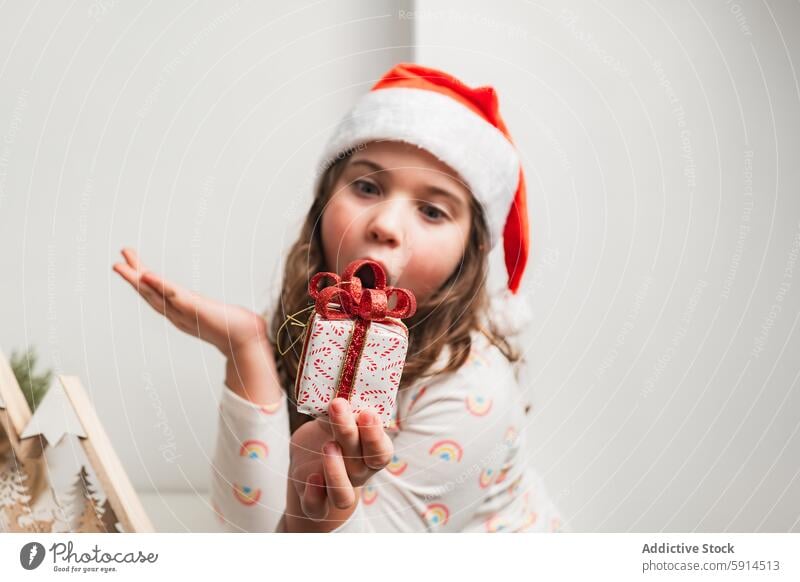 Junges Mädchen mit Weihnachtsmannmütze präsentiert ein kleines Weihnachtsgeschenk Weihnachten Weihnachtsmütze Geschenk präsentieren Lächeln festlich Feiertag