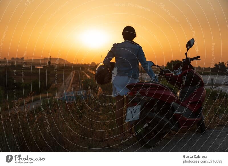 Frau mit Helm und Motorrad blickt auf den Horizont. Schutzhelm Sonnenaufgang - Morgendämmerung Außenaufnahme Lifestyle reisen Silhouette Farbfoto