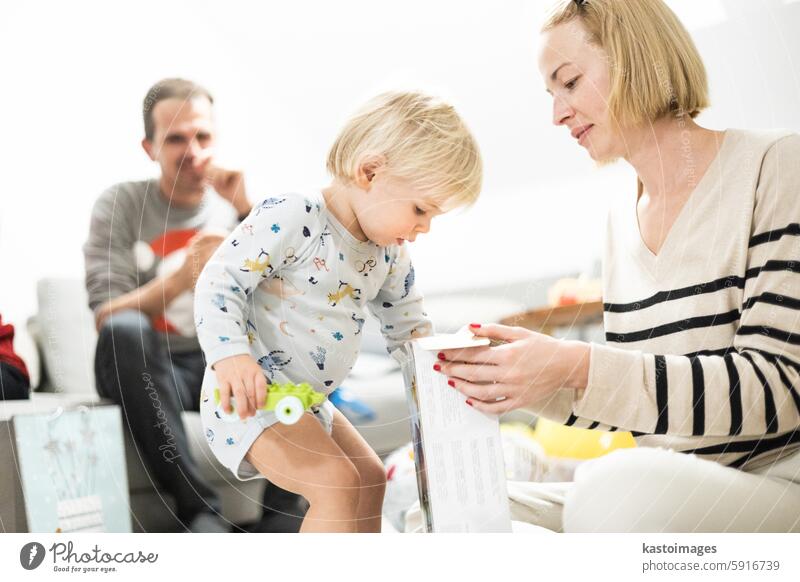 Niedliches kleines blondes kaukasisches Kleinkind packt Weihnachts- oder Geburtstagsgeschenk aus. Bezaubernder kleiner Säugling Baby Junge öffnet Geschenk Kind