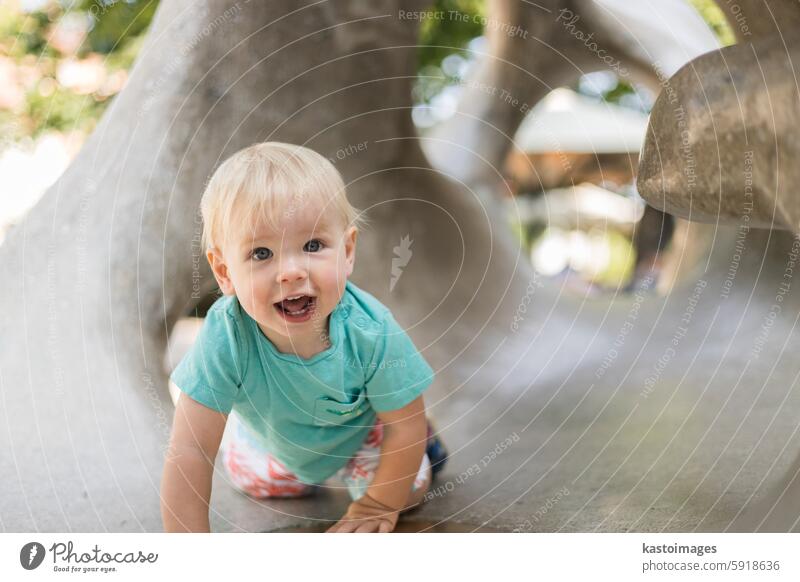 Kind spielt auf Spielplatz im Freien. Kleinkind spielt auf Schule oder Kindergarten Hof. Aktives Kind auf Stein gemeißelter Rutsche. Gesunde Sommeraktivität für Kinder. Kleiner Junge klettert im Freien.