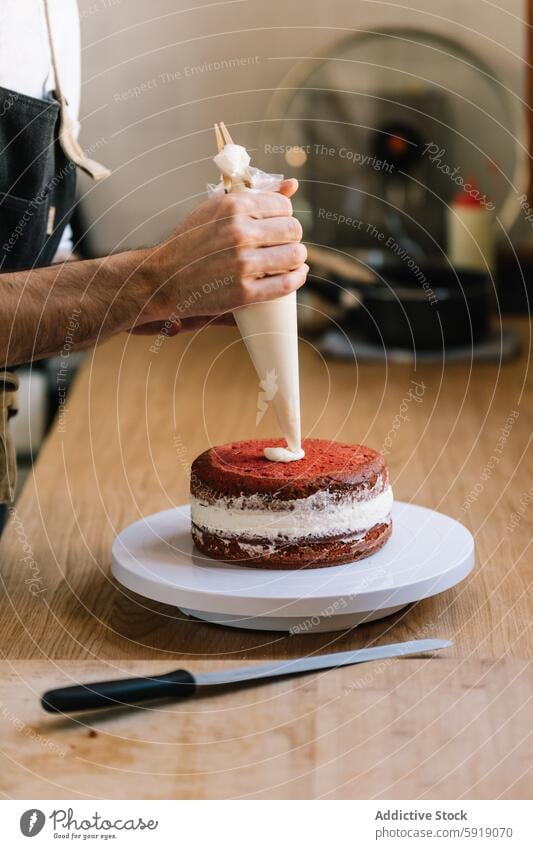 Männlicher Koch beim Verzieren einer roten Samttorte mit Sahne Küchenchef Kuchen roter Samt Spritzbeutel Dessert backen Essen zubereiten Zubereitung von Speisen