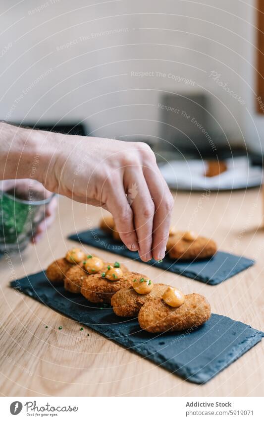 Abgeschnittene, nicht erkennbare Person, die Essen auf einer Schiefertafel garniert Hand Garnierung Lebensmittel Küche Krokette Saucen Schnittlauch kulinarisch