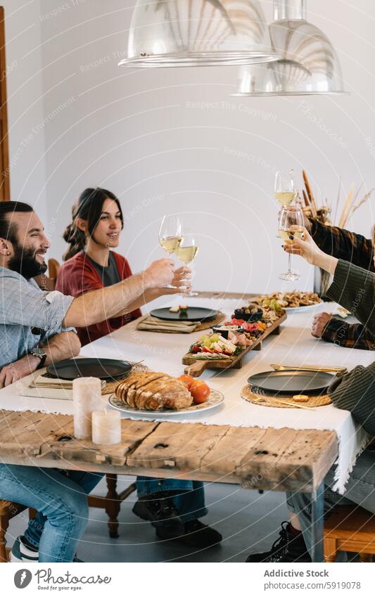 Freunde genießen eine gemeinsame Mahlzeit mit Wein in einer gemütlichen Umgebung Zuprosten heimwärts Tisch rustikal hölzern heiter Mann Frau Weißwein Abendessen