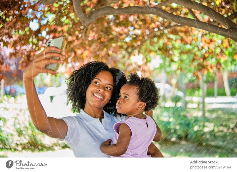 Mutter und Tochter machen ein Selfie unter einem Baum sonnig Freude Afroamerikaner schwarz ethnisch Eltern Kind Frau Kleinkind Mädchen Lächeln Glück