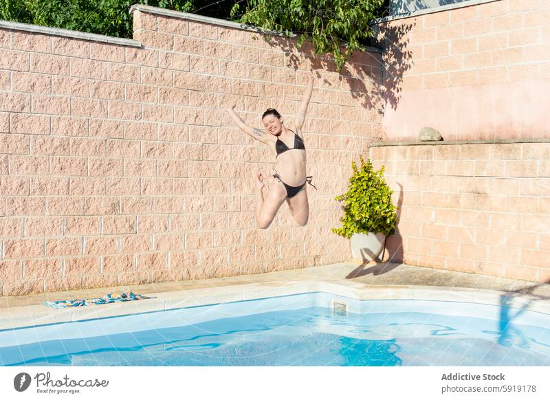 Junge Frau springt freudig in ein Schwimmbecken jung springend Schwimmbad Freude Sonnenlicht Sommer Spaß Freizeit Hinterhof im Freien Aktivität Badebekleidung