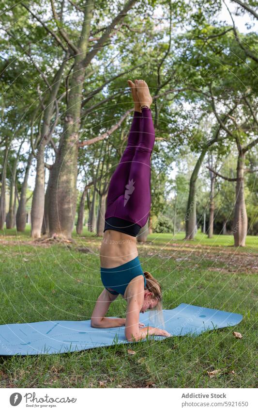 Schlanke Frau macht Eagle Legs Position im Kopfstand Pose im grünen Park Yoga Adlerbeine im Kopfstand üben Asana beweglich Gleichgewicht Vitalität Harmonie