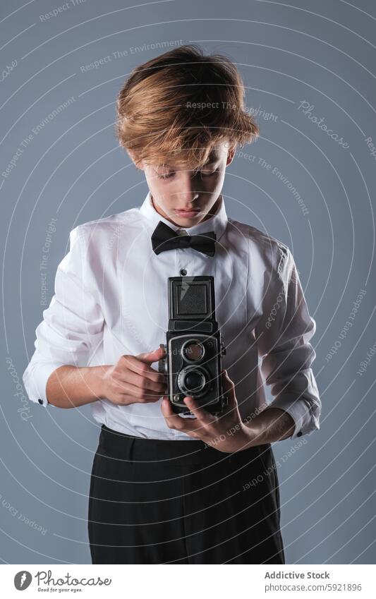 Preteen Junge in weißem Hemd und Fliege hält Vintage-Foto-Kamera digital Fotoapparat Gerät Kind Stil Outfit Mode modern Fotografie Kindheit Bekleidung anhaben