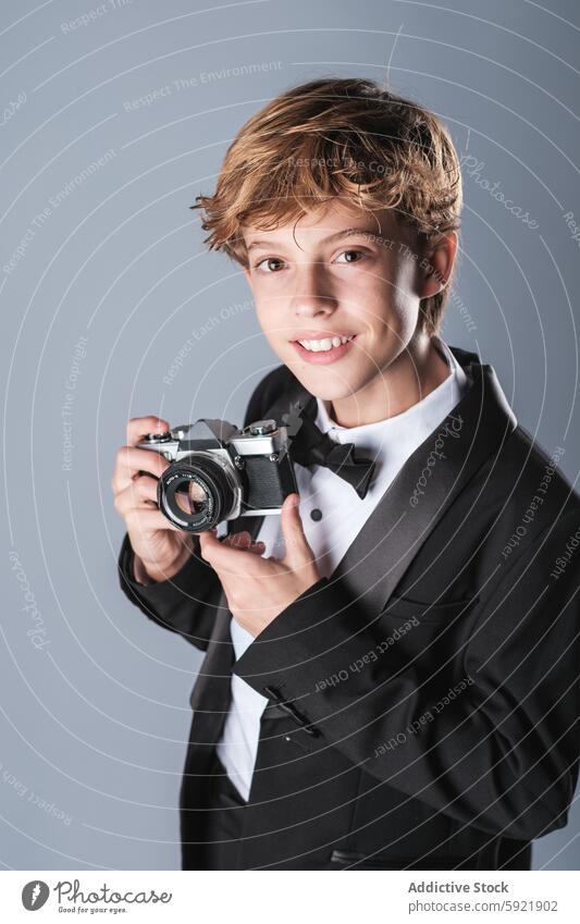 Jugendlicher in elegantem Anzug mit Fliege und Fotoapparat Junge Lächeln professionell digital Kind formal Outfit stilvoll Glück niedlich anhaben wenig