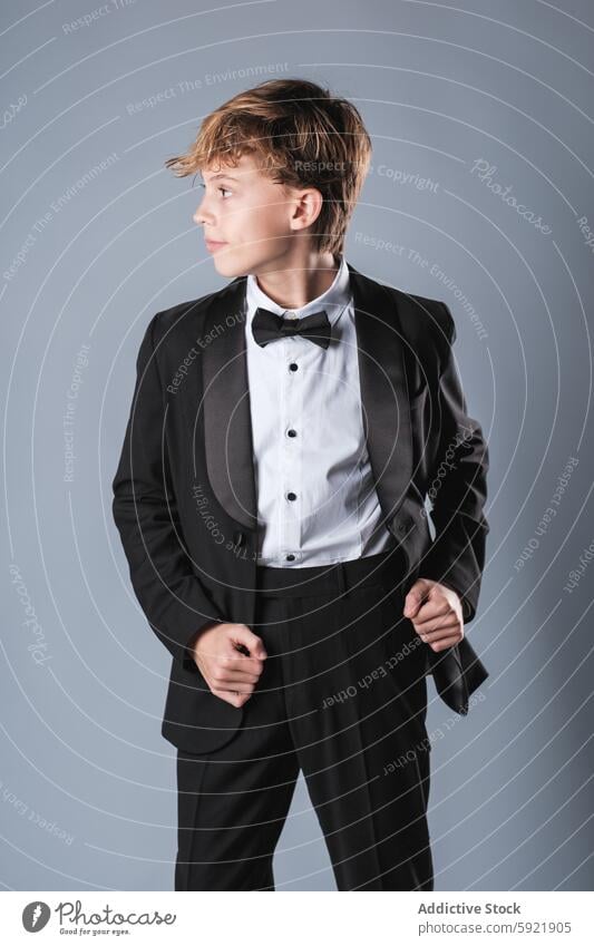 Jugendlicher im schwarzen Anzug und mit Fliege, der im Studio wegschaut Junge formal Kind stilvoll elegant selbstbewusst Stil Outfit gut gekleidet trendy