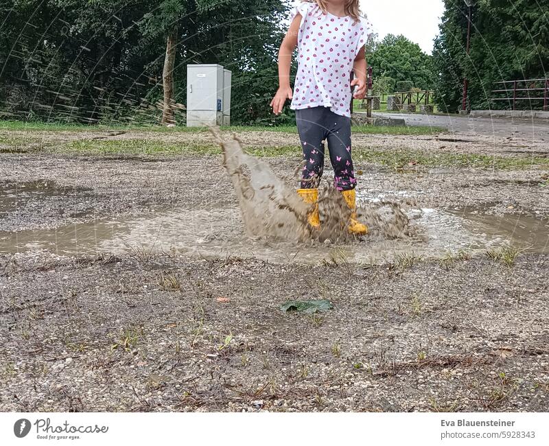 Kind springt in Pfütze springen sprung spritzen Gummistiefel Freude nass Wasser Regen Kindheit Fröhlichkeit Matsch matschig gatsch gelb hüpfen Wetter dreckig