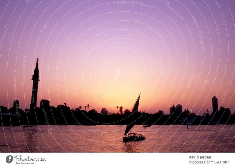 Silhouette einer ägyptischen Stadt mit Segelboot im Vordergrund und pastellrosa-lila farbenem Himmel, Sonnenuntergangsstimmung Skyline Skyline-Silhouette