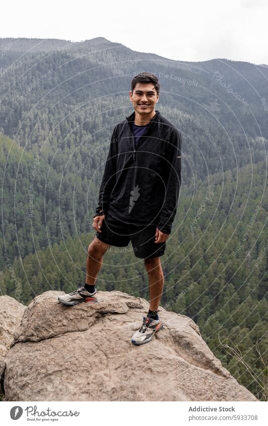 Mann lächelt, während er auf einem Waldfelsen steht wandern Felsen im Freien Natur lässig Stehen Lächeln in die Kamera schauen Gesundheit Freizeit Abenteuer