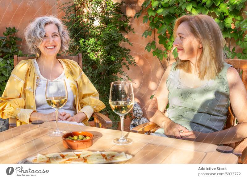 Zwei Frauen genießen Wein und Gespräche im Freien Lächeln sonnig Tisch Stuhl Garten Glas Freizeit Genuss Freundschaft Sommer tagsüber friedlich entspannend