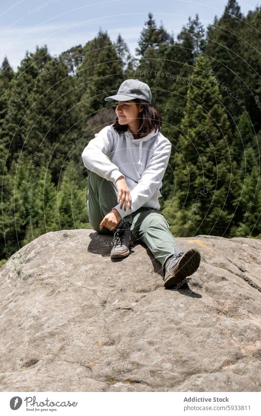 Frau sitzt auf einem Felsen mit Blick auf die Waldlandschaft Natur Sitzen Freizeitkleidung Kapuzenpulli Hose im Freien Gelassenheit beschaulich Grün Landschaft