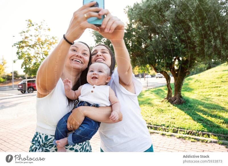 Lesbisches Paar macht Selfie mit ihrem kleinen Sohn im Freien lesbisch Baby Familie Smartphone Freude Fröhlichkeit Liebe Eltern Frau Sommer Sonnenlicht Park