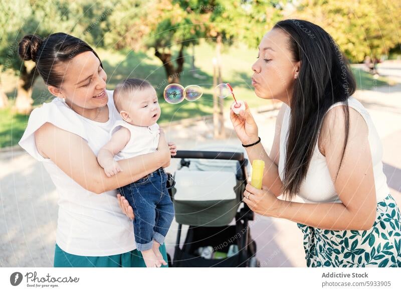 Lesbisches Paar genießt einen Tag mit ihrem Sohn beim Blasen von Seifenblasen lesbisch Frau Baby Mutter Park qualitätsvolle Zeit blasend Beteiligung zuschauend