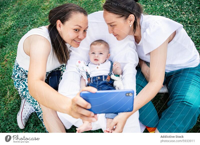 Lesbische Familie, die ein Selfie mit einem kleinen Jungen auf einer Wiese macht und dabei lächelt und sich freut kolumbianisch Paar lesbisch lgbt Baby Freude