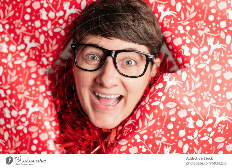 Frau mit freudigem Gesichtsausdruck, eingewickelt in eine festliche rote Weihnachtsdecke Weihnachten Aufregung Freude Decke Feiertag Muster Brille Ausdruck