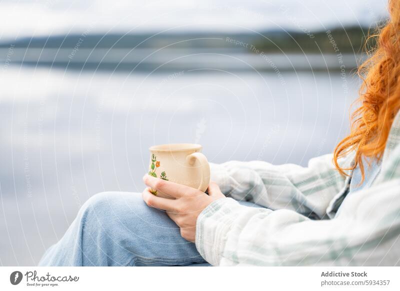 Person hält einen Becher an einem ruhigen See beim Camping Morgen Ruhe Frieden Erholung Rotschopf Jeansstoff Plaid Bekleidung Keramik Natur im Freien Freizeit