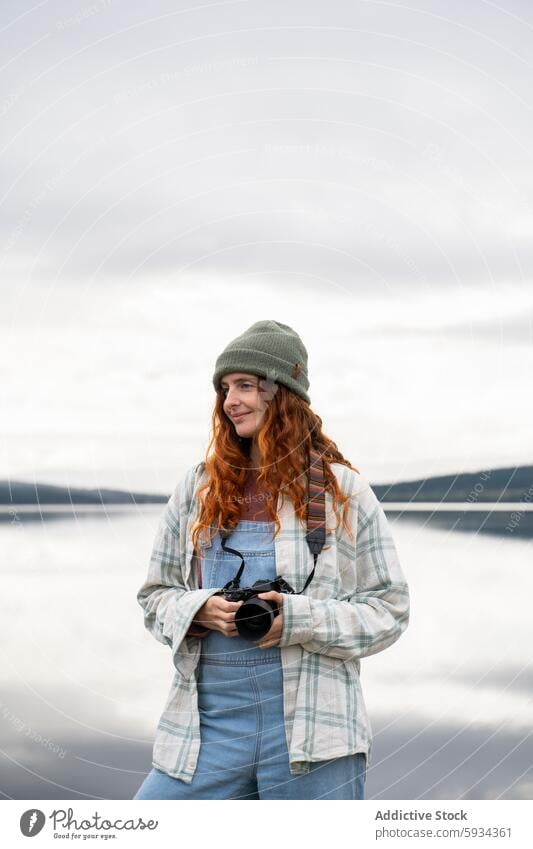 Junge Frau genießt die Fotografie auf einem Campingplatz am See Natur im Freien lässig Rotschopf krause Haare Jeansstoff Latzhose Beanie ruhig Freizeit Hobby