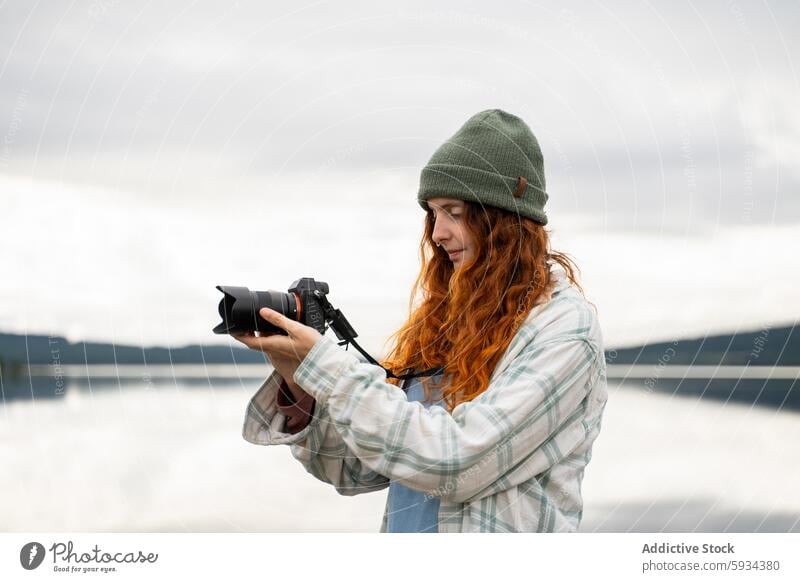 Junge Frau beim Fotografieren einer ruhigen Seeszene Fotokamera Natur im Freien Gelassenheit jung einfangen grüne Mütze karierte Jacke malerisch Landschaft Ruhe