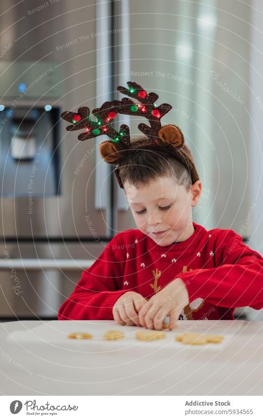 Junge im festlichen Weihnachtspulli beim Plätzchenverzieren Essen zubereiten Weihnachten Keks dekorierend Pullover Rentier Geweih Stirnband Feiertag Küche Fokus