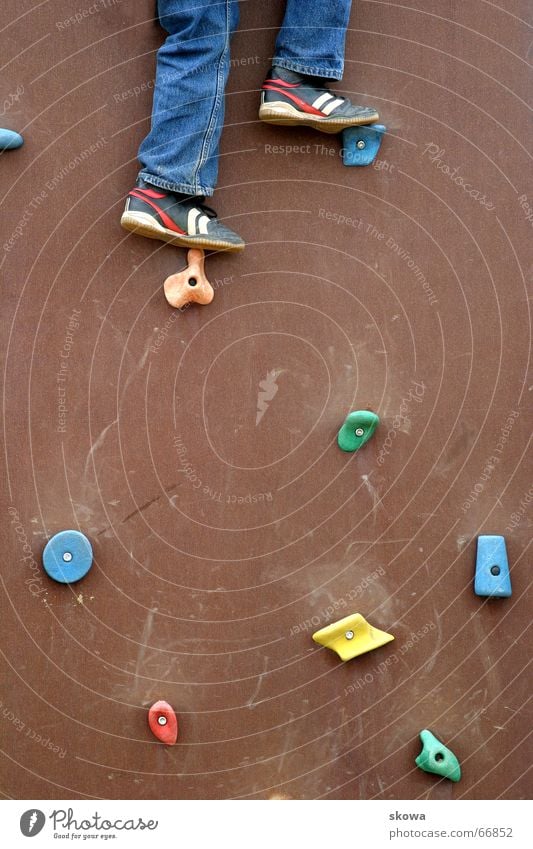 bergsteigen auf'm Spielplatz Kletterwand mehrfarbig Schuhe Geschicklichkeit braun Hose Wand Klettern Beine hoch Jeanshose