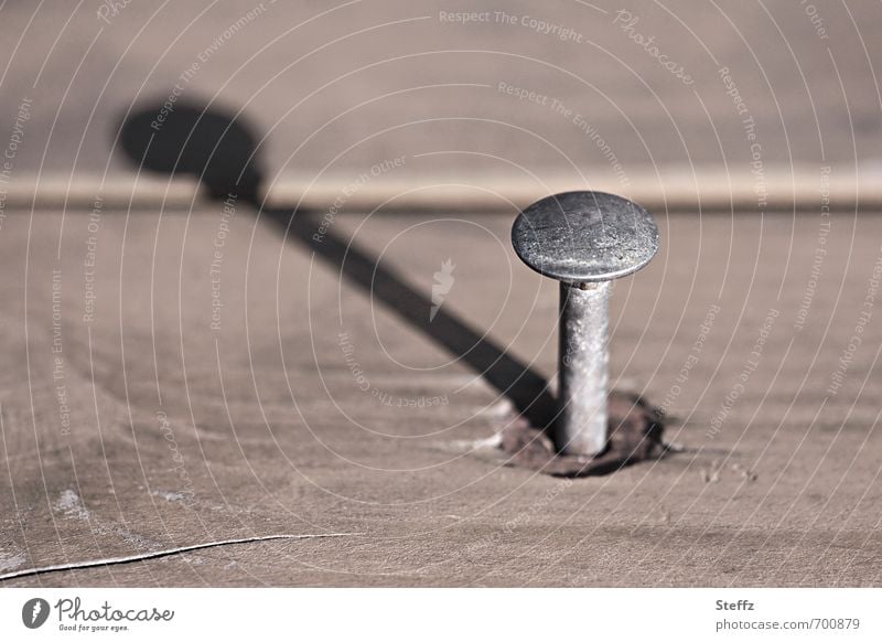 ein Nagel wie eine Sonnenuhr Nagelkopf Metall Holz reparieren einfach Schattenspiel Zeitmessung Schattenseite nageln beige Holzbrett Handwerk einzeln