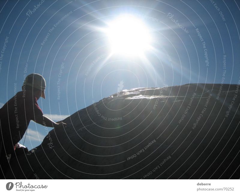 Die Silhouette eines kleinen Jungen, der mit der Sonne und dem blauen Himmel im Rücken auf einen Felsbrocken klettert. Hügel Kind steigen weiß grau hart