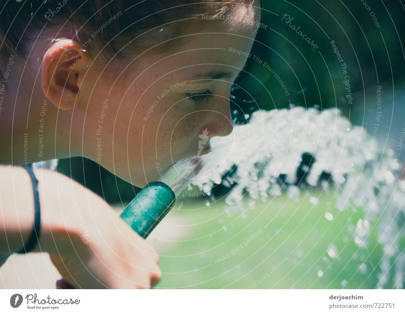 Ein Mädchen hält einen Wasserschlauch in der Hand. Sie trinkt aus dem heraus strömenden Waser daraus. .Quench trinken Wohlgefühl Sommer feminin Mund 1 Mensch