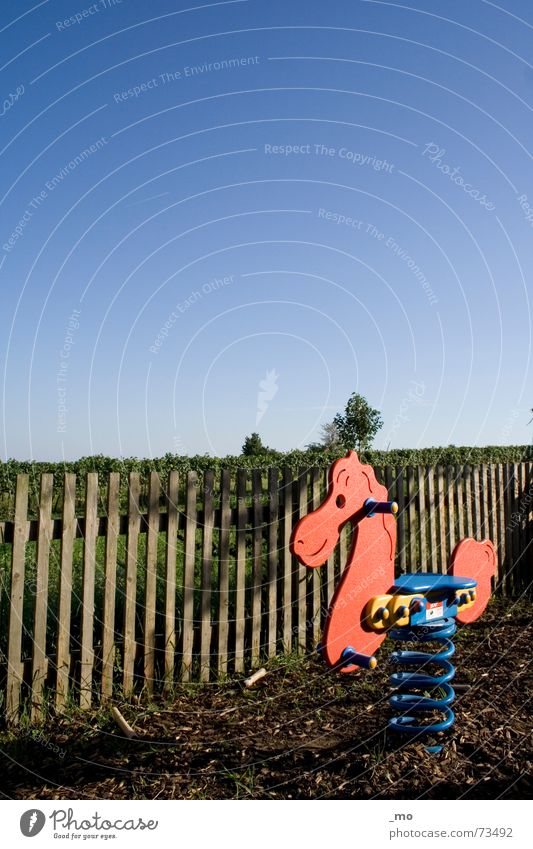 Ritt auf dem Vulkan Spielplatz Spielen Österreich Pferd Spielzeug Zaun Holzbrett Schaukel Schaukelpferd Einsamkeit ungestört Reitsport pferdeschaukel Himmel