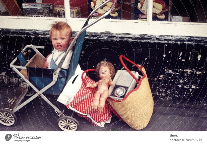 Exile on Main Street Blick Kind Kleinkind Mädchen Arme Kleinstadt Verkehrsmittel Straße Kinderwagen Tasche blond Spielzeug Puppe fahren Traurigkeit warten