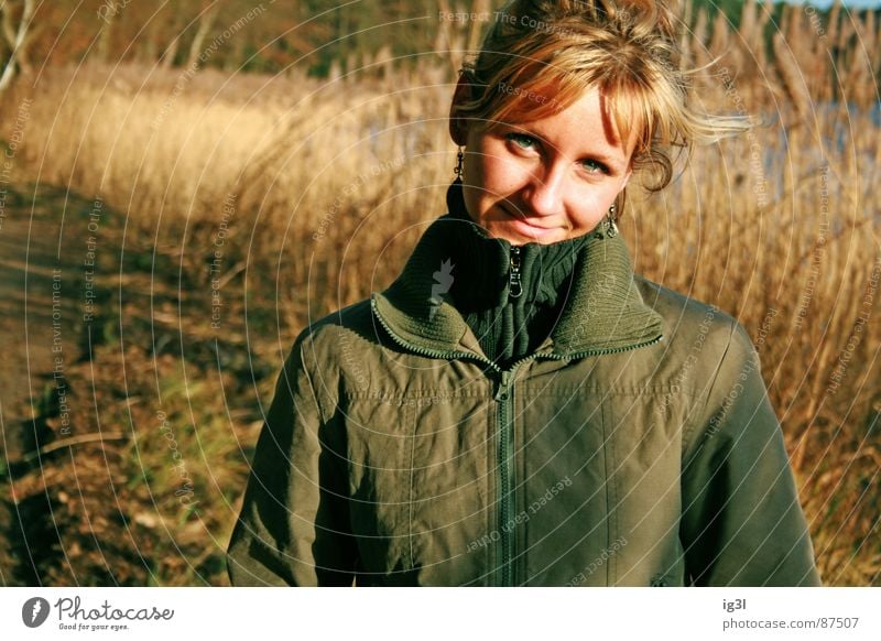 nach 5 am See Sonnenstand Frau feminin Jacke Abenddämmerung Herbst springen Frühlingsgefühle Schilfrohr Gras Außenaufnahme grinsen Gefühle Erwartung grün gelb