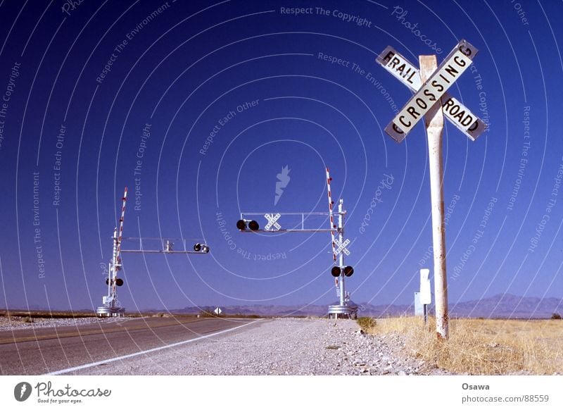 irgendwo in Arizona Steppe Schranke Gleise weiß Asphalt Gras trocken Ampel Bahnübergang Eisenbahn Verkehr Straßennamenschild USA Wüste Bahnschranke Himmel blau