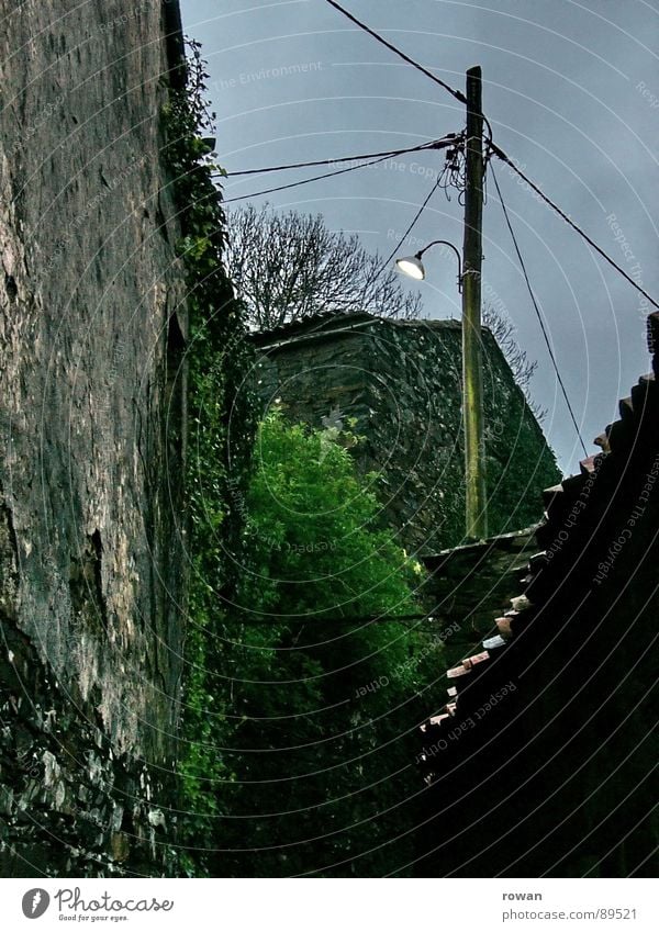 Dämmerung Dorf Laterne Licht dunkel Nacht Mauer Haus halbdunkel Wolken schlechtes Wetter Elektrizität Strommast Einsamkeit leer trist Efeu Vergangenheit Verfall