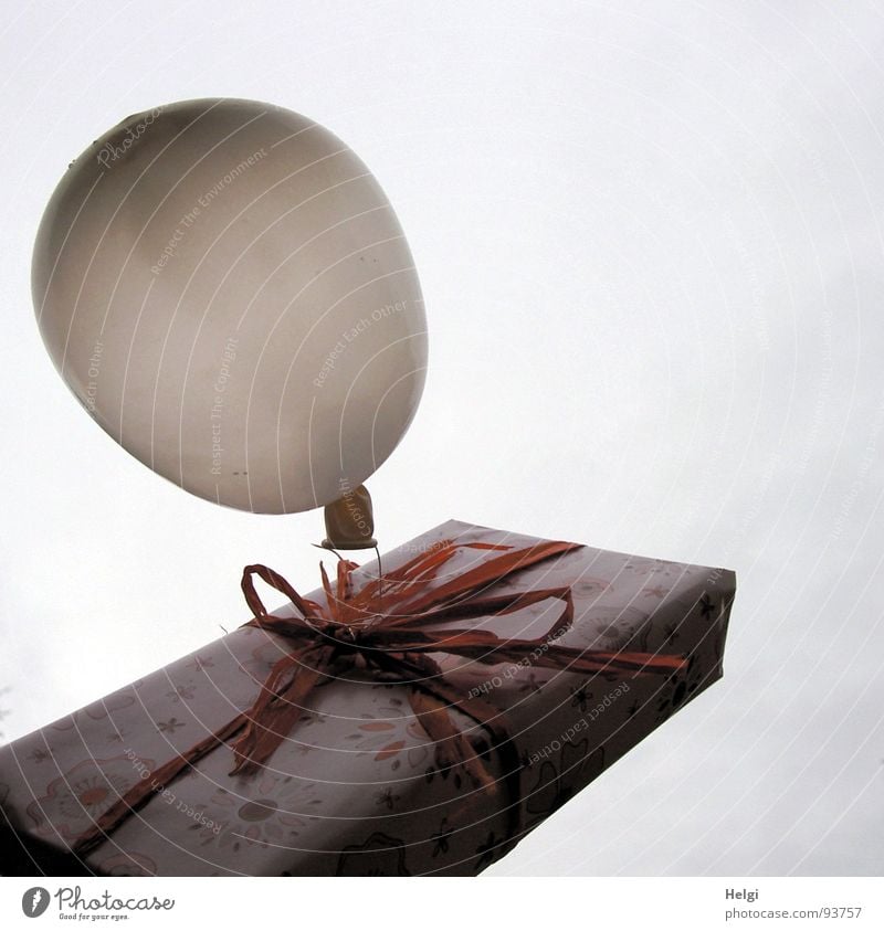 verpacktes Geschenk in rosa gemustertem Papier mit rosa Schleife und einem Luftballon vor grauem Himmel Gedeckte Farben Außenaufnahme Detailaufnahme