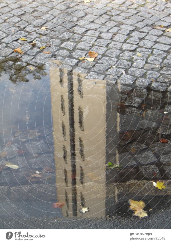 Wolkenkratzend. Geerdet. Hochhaus Reflexion & Spiegelung Pfütze Kopfsteinpflaster grau Wasser