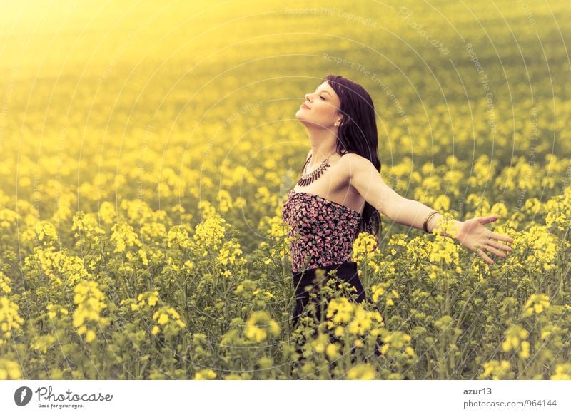 Schöne junge Frau im Sommer Glück auf gelber Wiese aus Raps bis zum Horizont. Hübsches Mädchen mit Lebensfreude geniesst die Sonnenschein Pause und das Leben. Erholung und Energie tanken vom Zeit Umwelt Stress in der Natur Idylle.