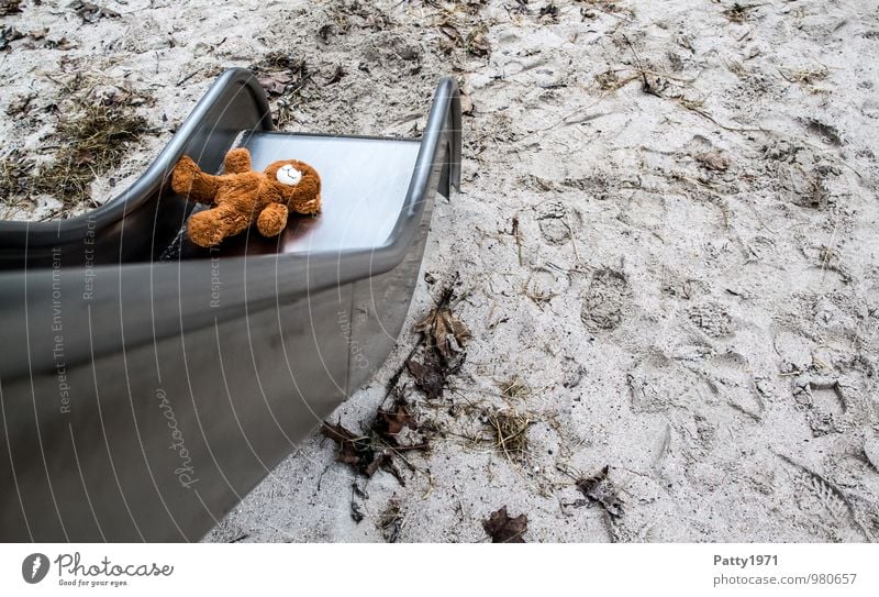 Verlorener / vergessener Teddybär liegt auf einer Kinderrutsche auf einem Spielplatz. Spielen Spielzeug Rutsche Stofftiere Sand Metall Fußspur liegen