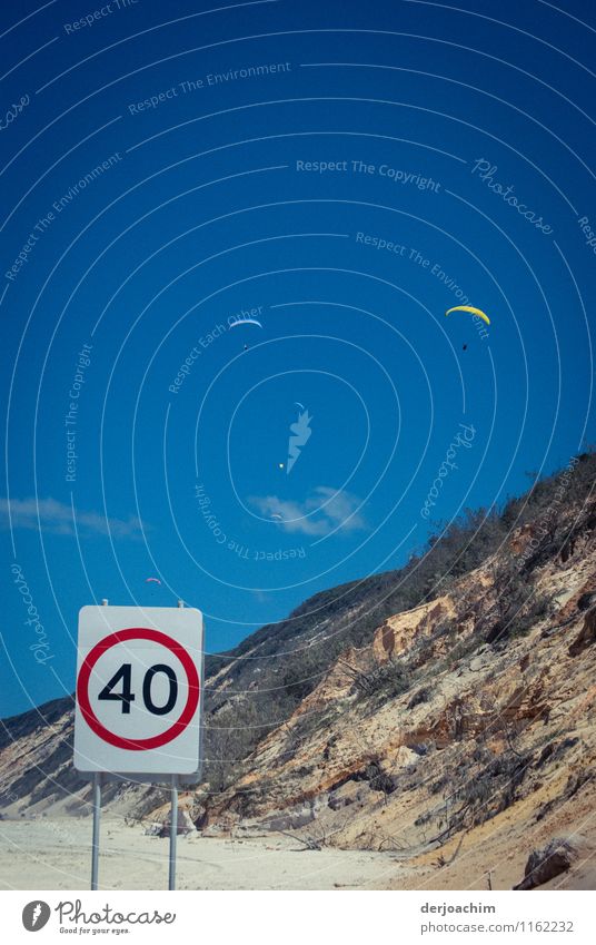 Paraglider pilots hover in, on the steep coast at Rainbow Beach. Top speed sign for cars 40 km stands at the beach .Queensland / Australia Joy Harmonious