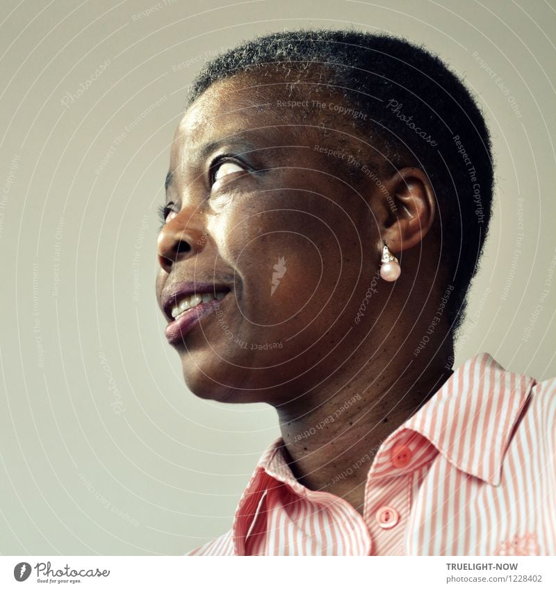 Beautiful African woman from Togo with very short hair, slightly opened mouth, one earring with pearl in a white and pink striped fine shirt with collar from below in half profile