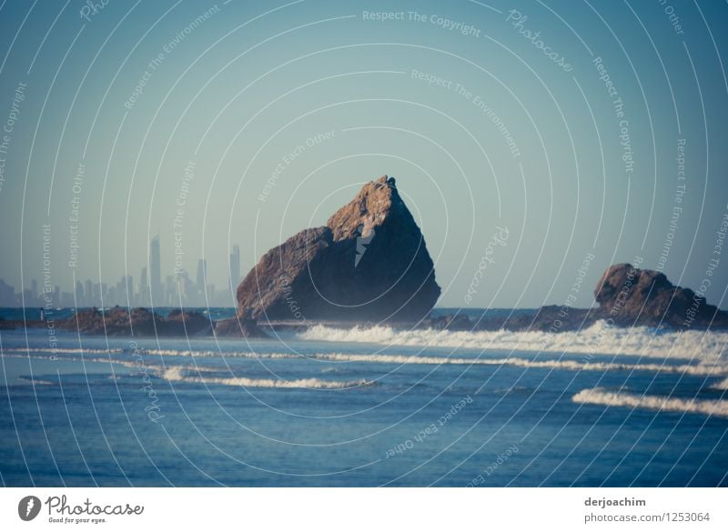 Big chunk. Huge rock lies in the Pacific surf. Queensland. Australia. In the background very small : skyscrapers. Exotic Calm Trip Summer Beach Environment